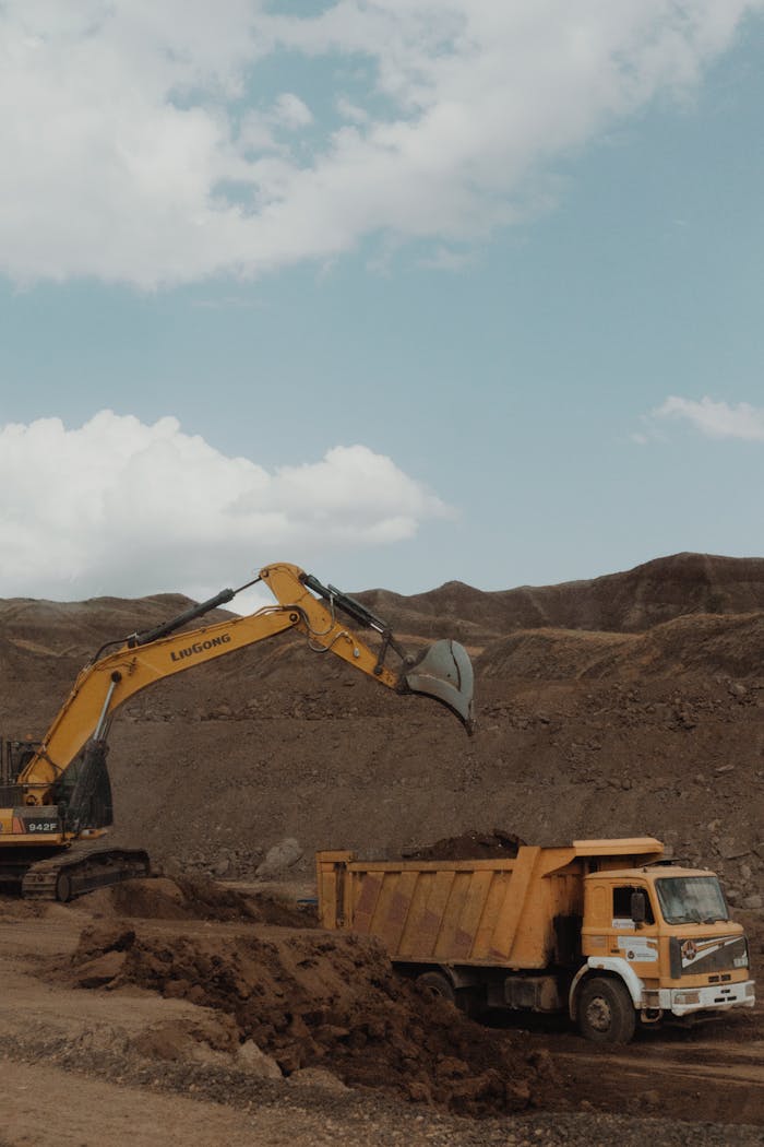 Yellow excavator and dump truck operating in a mining setting under a blue sky.